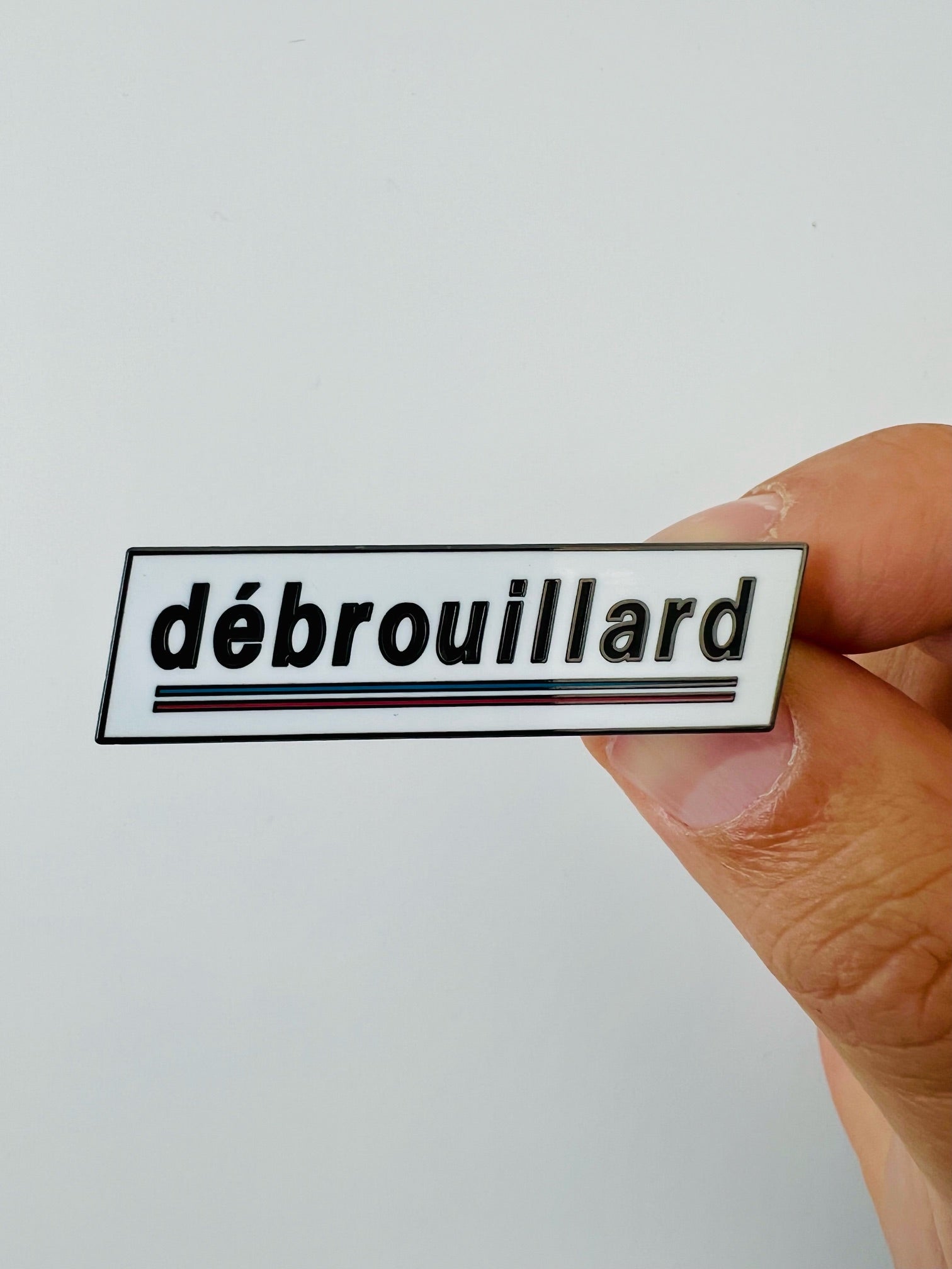 Hand holding a white pin with the 'débrouillard' logo